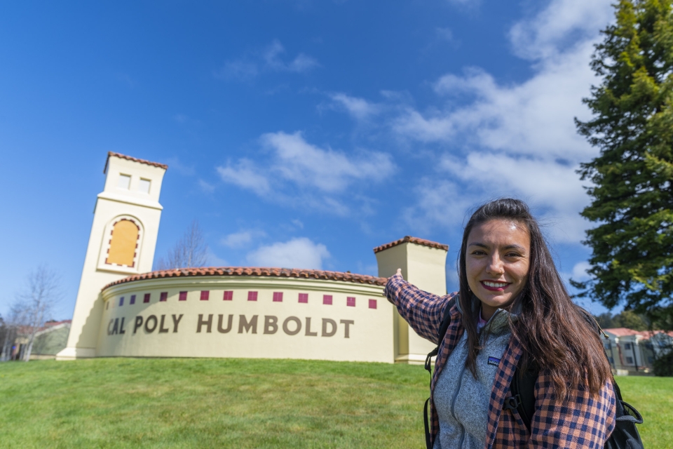 Wildlife major and transfer student sharing a smile in front of the Cal Poly Humboldt sign